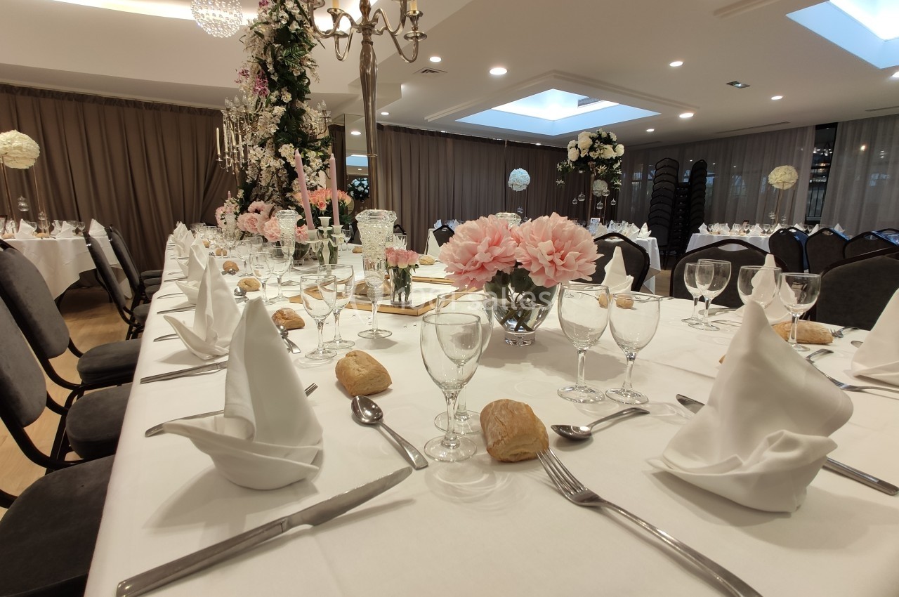 Table élégamment dressée pour un événement, avec serviettes pliées, verres, couverts et décorations florales.