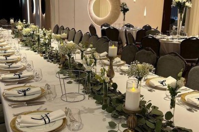 Salle de réception élégante avec tables rondes dressées, chaises transparentes et décorations florales.