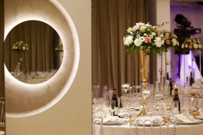 Salle de réception élégante avec tables rondes dressées, chaises transparentes et décorations florales.