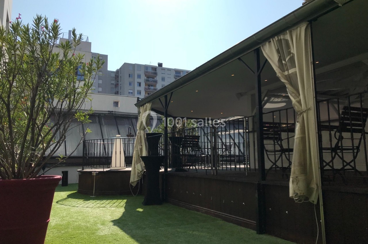 Terrasse extérieure avec pergola, chaises et table sur un sol en gazon synthétique, entourée de bâtiments urbains.