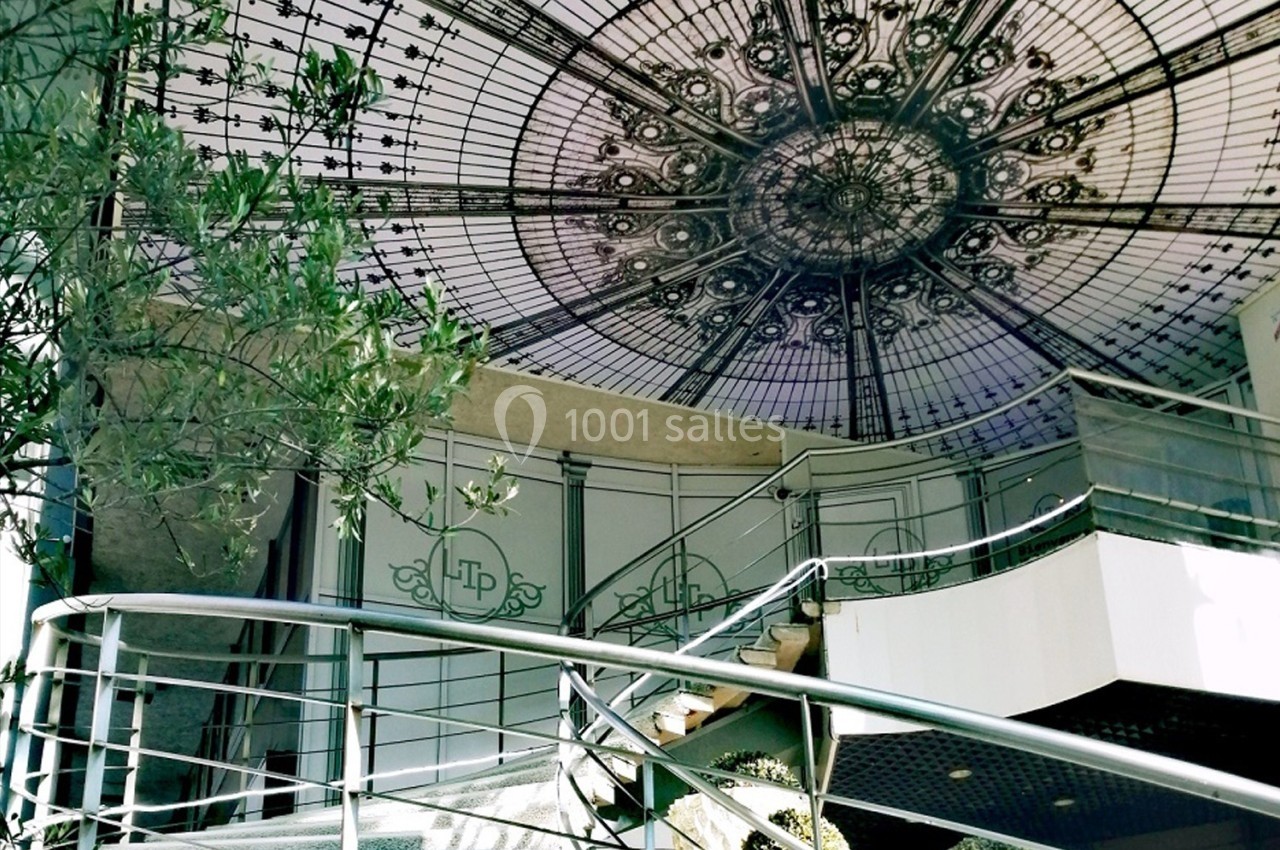 Escalier en colimaçon menant à une verrière ornée de motifs géométriques et végétaux, entourée de verdure.