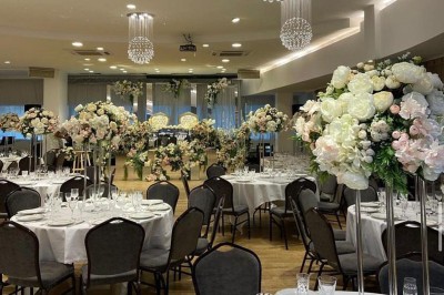 Salle de réception élégante avec tables rondes dressées, chaises transparentes et décorations florales.