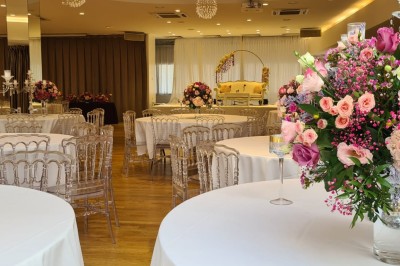 Salle de réception élégante avec tables rondes dressées, chaises transparentes et décorations florales.