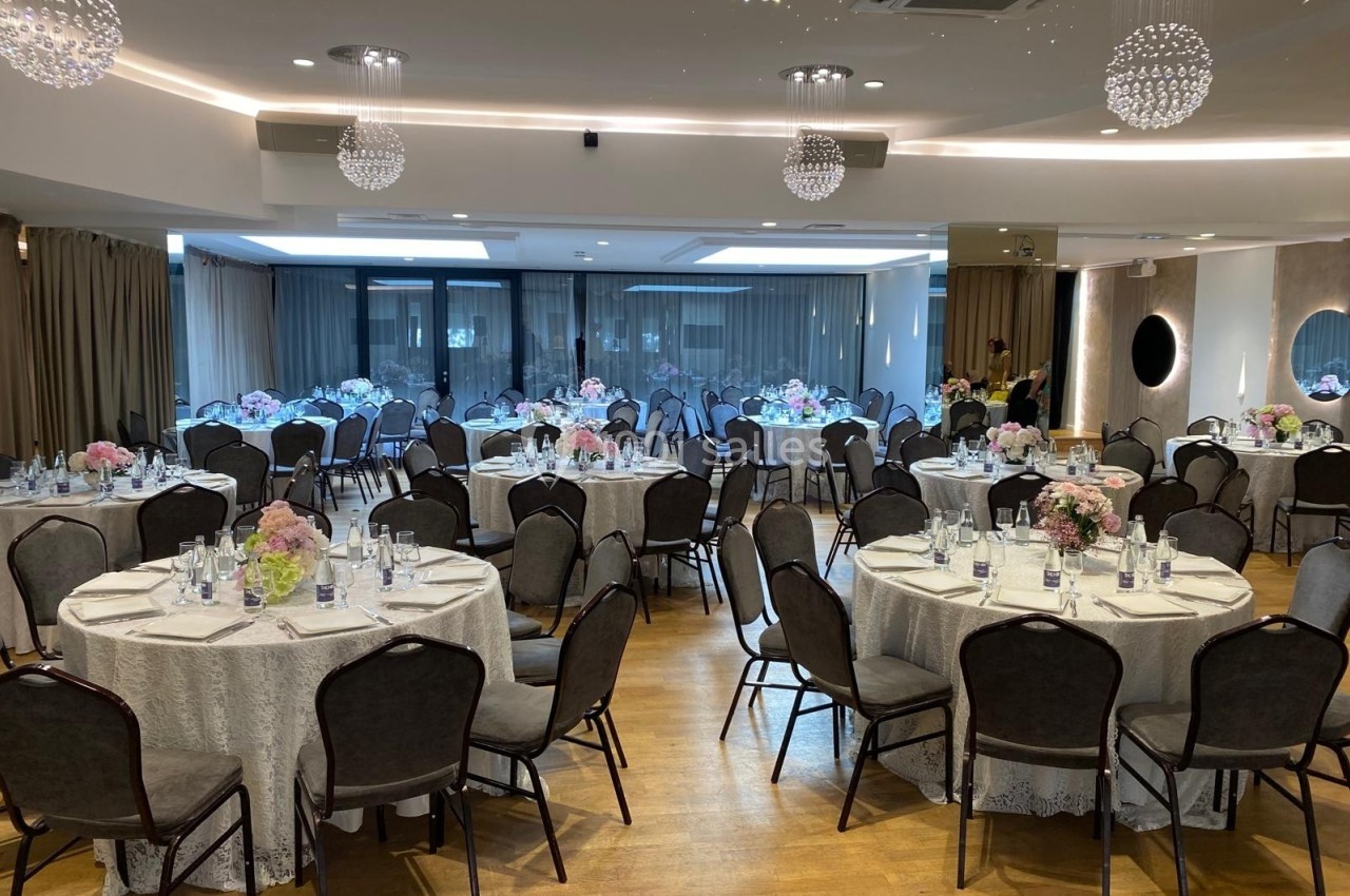 Salle de réception élégante avec tables rondes décorées de nappes blanches, fleurs et chaises noires.