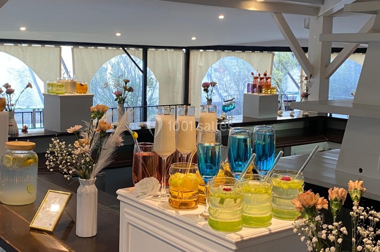 Buffet de boissons colorées avec des verres remplis de cocktails et décorations florales dans un espace lumineux.