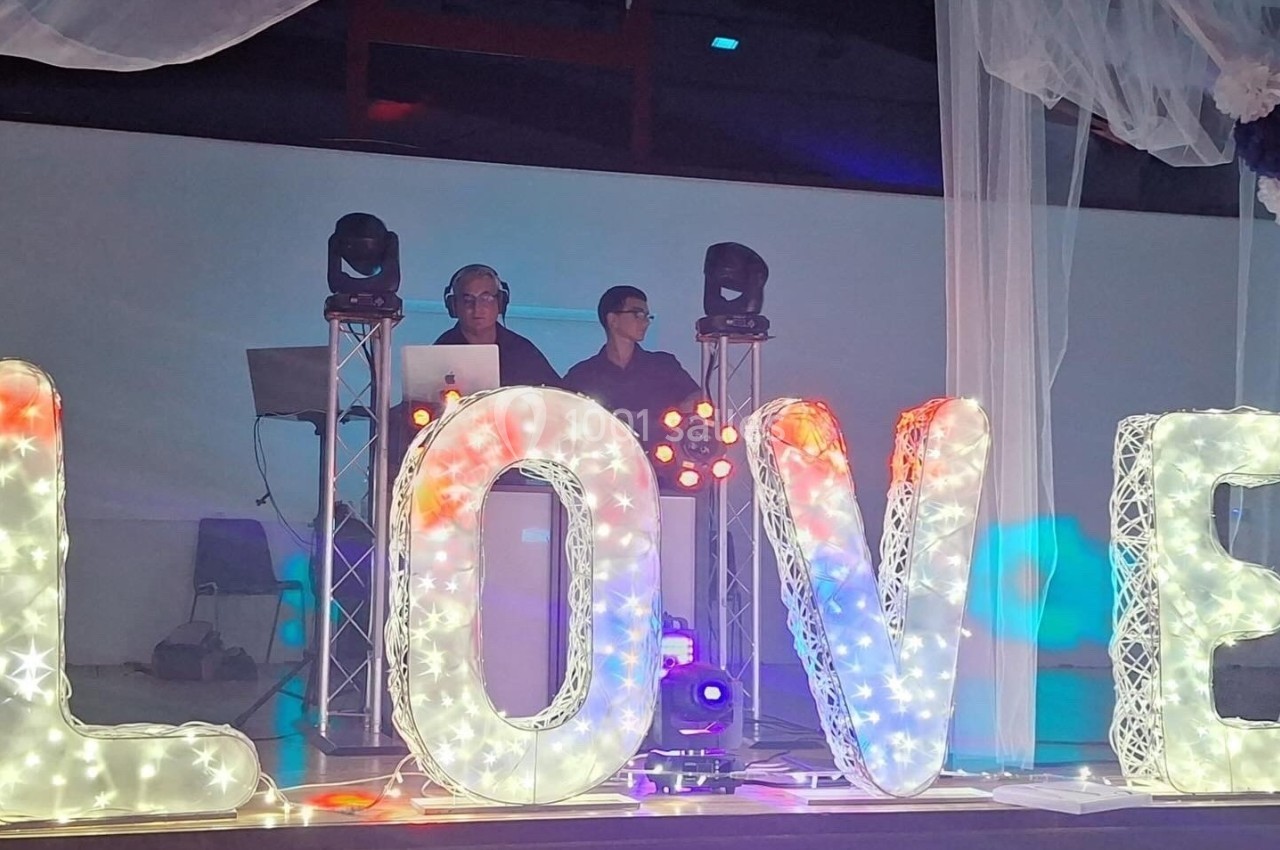 Deux DJ derrière une table de mixage, entourés de grandes lettres lumineuses formant le mot ’LOVE’.