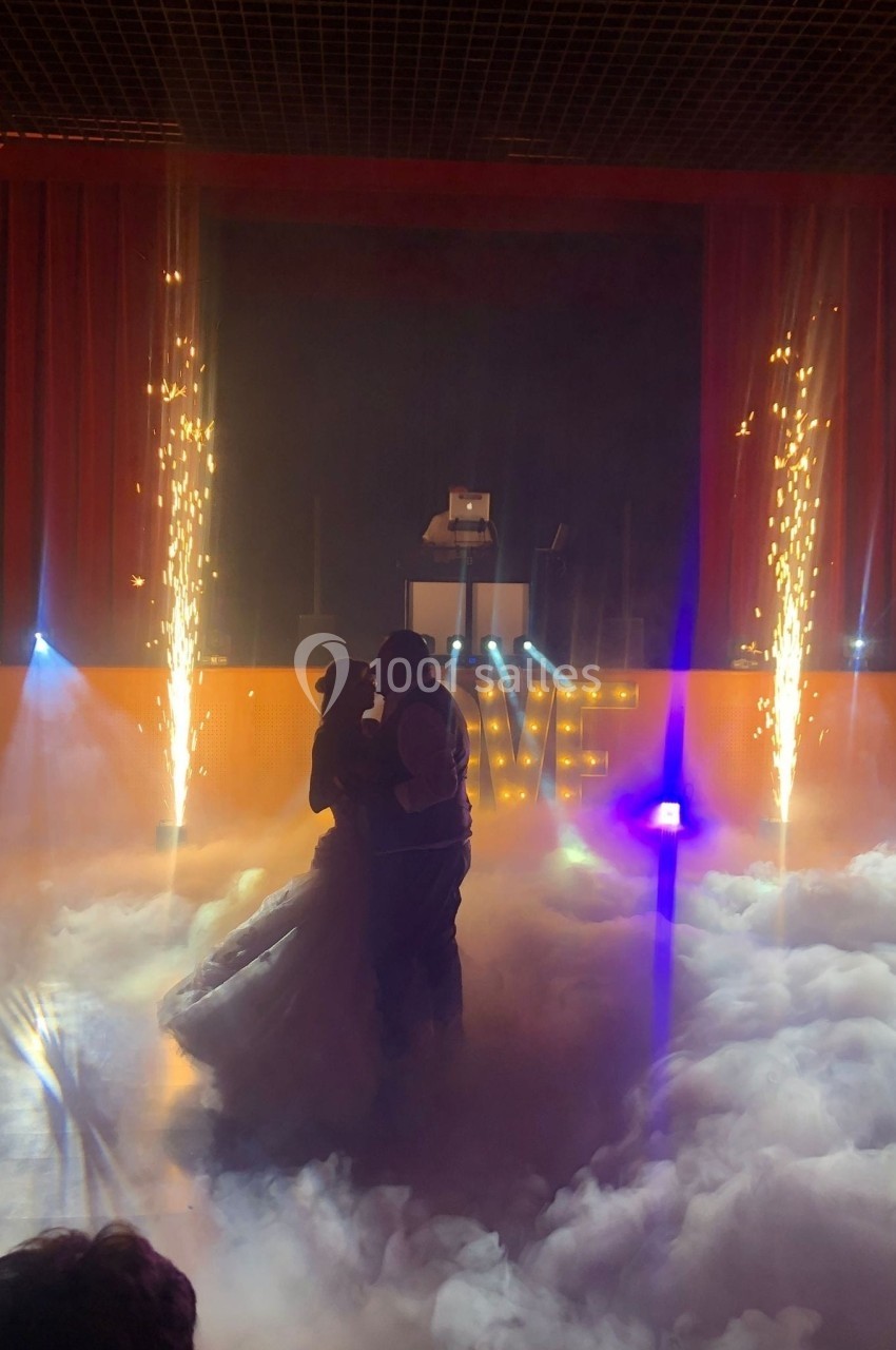 Un couple danse au milieu d'une scène enveloppée de fumée, avec des étincelles et des lumières en arrière-plan.