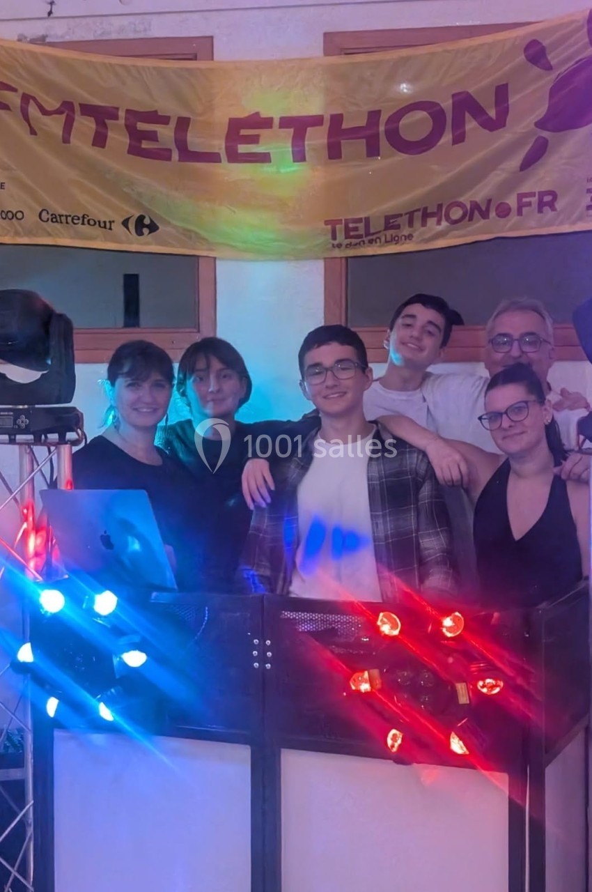 Un groupe de personnes souriantes posant devant une bannière du Téléthon, entourées d'équipements lumineux.