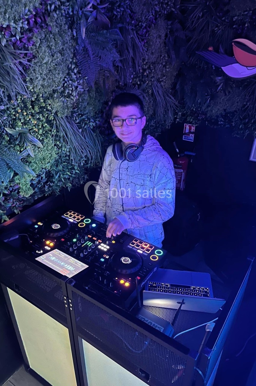 Un DJ mixe de la musique sur une table de mixage dans un espace décoré de plantes vertes.
