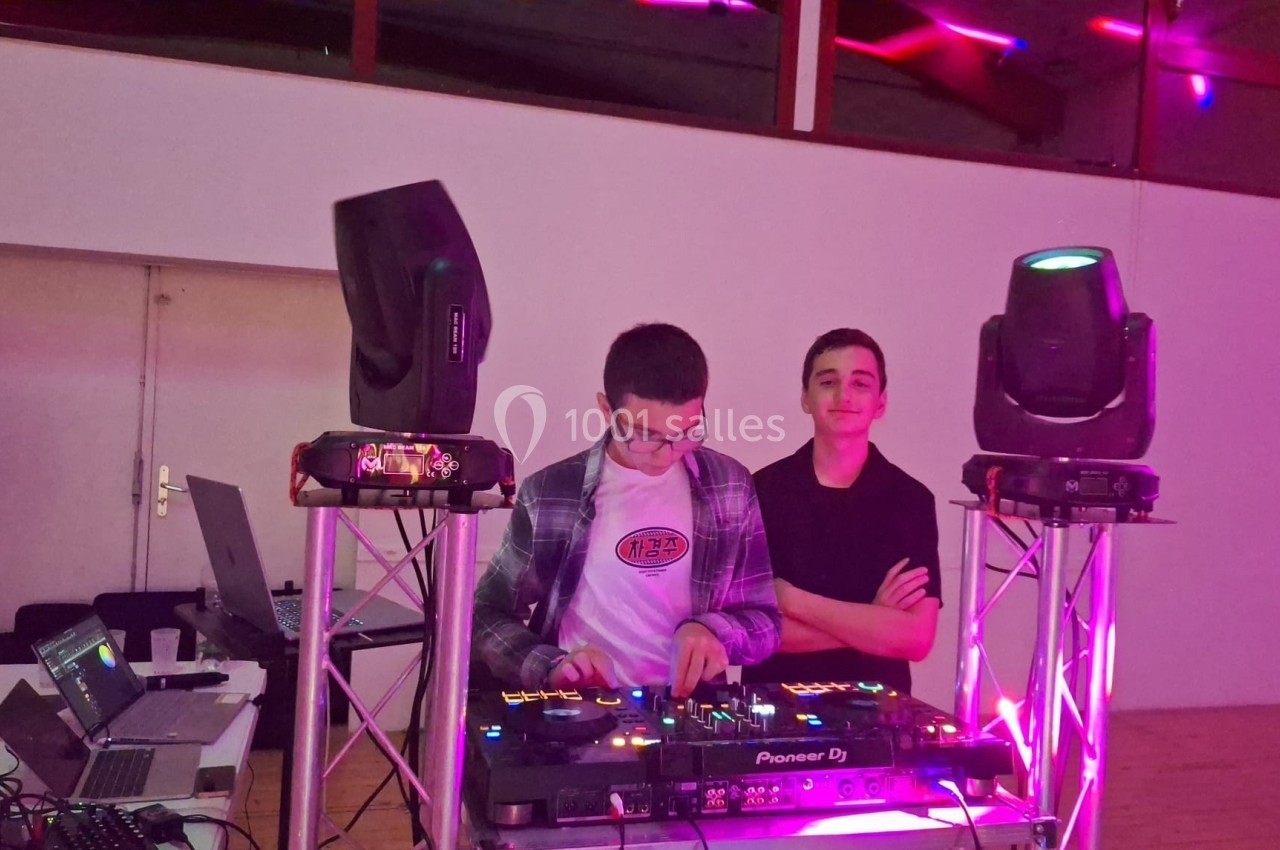 Deux personnes devant une table de mixage avec des lumières colorées et des enceintes dans une salle.