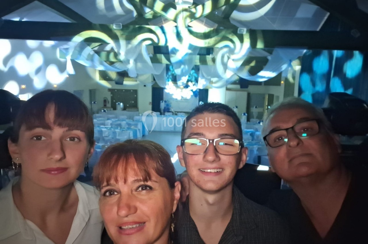Quatre personnes posent pour une photo dans une salle décorée avec des lumières et des tables dressées en arrière-plan.