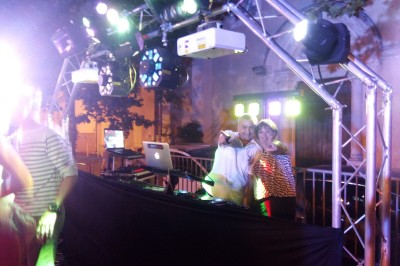 Installation de matériel de sonorisation et d'éclairage devant un mur en pierre, avec une personne debout à droite.