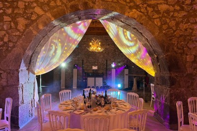 Installation de matériel de sonorisation et d'éclairage devant un mur en pierre, avec une personne debout à droite.
