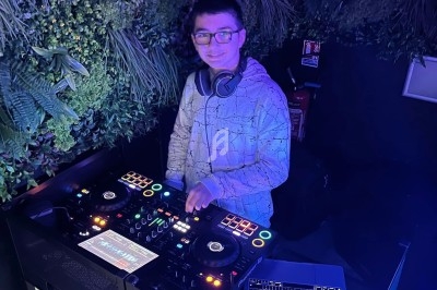 Un DJ mixe sur une console dans un espace décoré de plantes murales et éclairé par des lumières colorées.