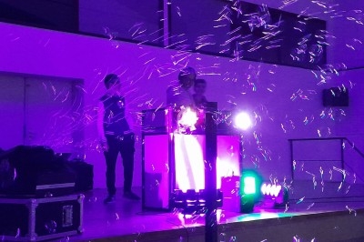 Un DJ anime une soirée sur scène avec des lumières violettes et des bulles flottant dans l'air.
