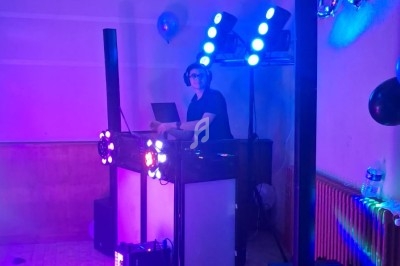 Un DJ mixe de la musique sur une scène éclairée par des lumières colorées dans une salle de fête.