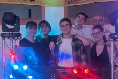Un groupe de personnes souriantes posant devant une table de mixage et une bannière du Téléthon.