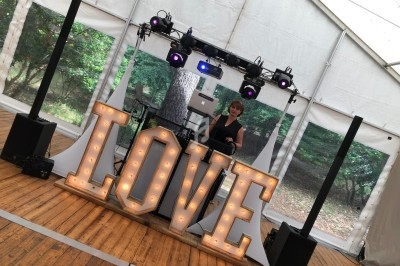 DJ animant un événement sous une tente, avec des lettres lumineuses formant le mot ’LOVE’ au premier plan.