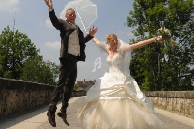 Un couple de mariés saute joyeusement sur un pont pavé par une journée ensoleillée.