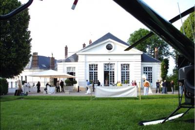 Salle décorée pour un événement avec un piano au premier plan, des chaises rouges alignées et des arrangements floraux.