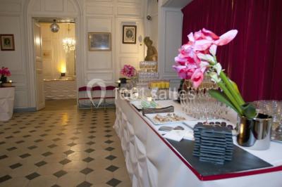 Salle décorée pour un événement avec un piano au premier plan, des chaises rouges alignées et des arrangements floraux.