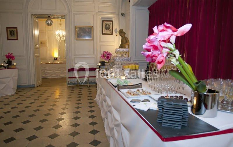 Table dressée avec des boissons, des fleurs et des amuse-bouches dans une salle élégante au sol en damier.