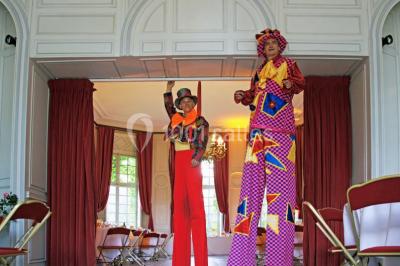 Salle décorée pour un événement avec un piano au premier plan, des chaises rouges alignées et des arrangements floraux.