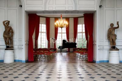 Salle décorée pour un événement avec un piano au premier plan, des chaises rouges alignées et des arrangements floraux.