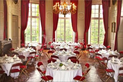 Salle décorée pour un événement avec un piano au premier plan, des chaises rouges alignées et des arrangements floraux.