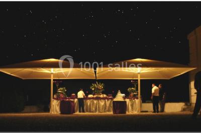 Salle décorée pour un événement avec un piano au premier plan, des chaises rouges alignées et des arrangements floraux.