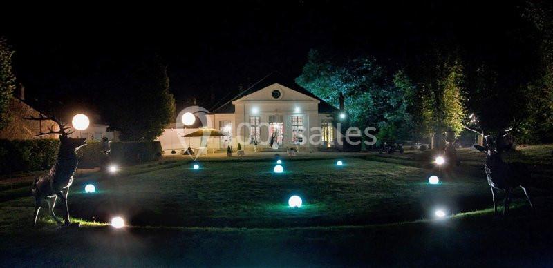 Jardin nocturne illuminé avec des sculptures de cerfs et des sphères lumineuses devant un bâtiment éclairé.