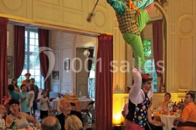 Salle décorée pour un événement avec un piano au premier plan, des chaises rouges alignées et des arrangements floraux.