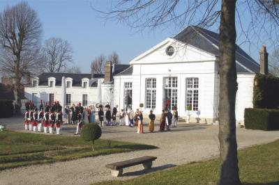 Salle décorée pour un événement avec un piano au premier plan, des chaises rouges alignées et des arrangements floraux.