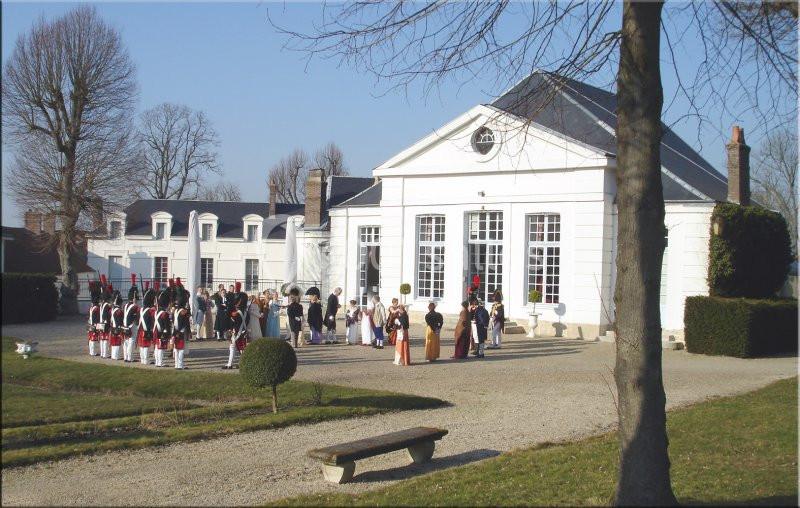 Groupe de personnes en costumes historiques devant un bâtiment blanc avec des arbres en arrière-plan.