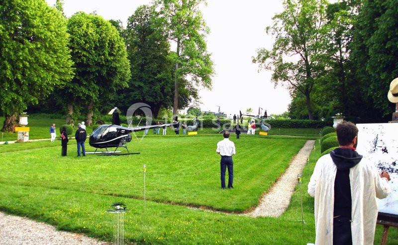 Un hélicoptère posé sur une pelouse entourée de personnes dans un jardin arboré.