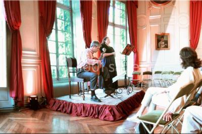 Salle décorée pour un événement avec un piano au premier plan, des chaises rouges alignées et des arrangements floraux.