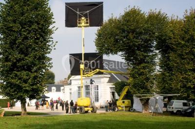 Salle décorée pour un événement avec un piano au premier plan, des chaises rouges alignées et des arrangements floraux.