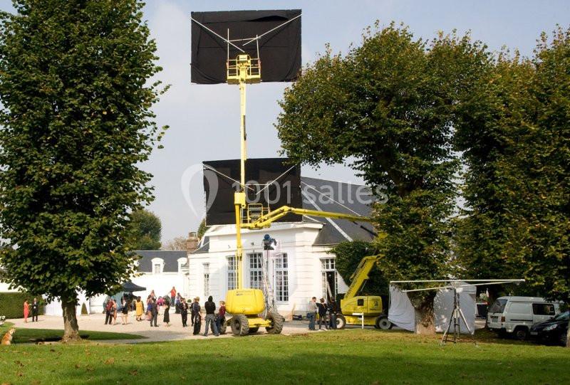 Tournage en extérieur devant un bâtiment blanc, avec équipements de cinéma et techniciens sur place.