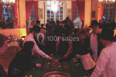 Salle décorée pour un événement avec un piano au premier plan, des chaises rouges alignées et des arrangements floraux.