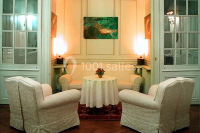 Salle décorée pour un événement avec un piano au premier plan, des chaises rouges alignées et des arrangements floraux.