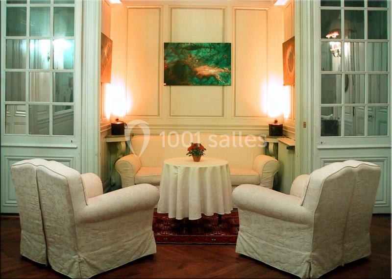 Salon élégant avec trois fauteuils, une table ronde ornée d'une plante, éclairé par des lampes murales et encadré de portes…