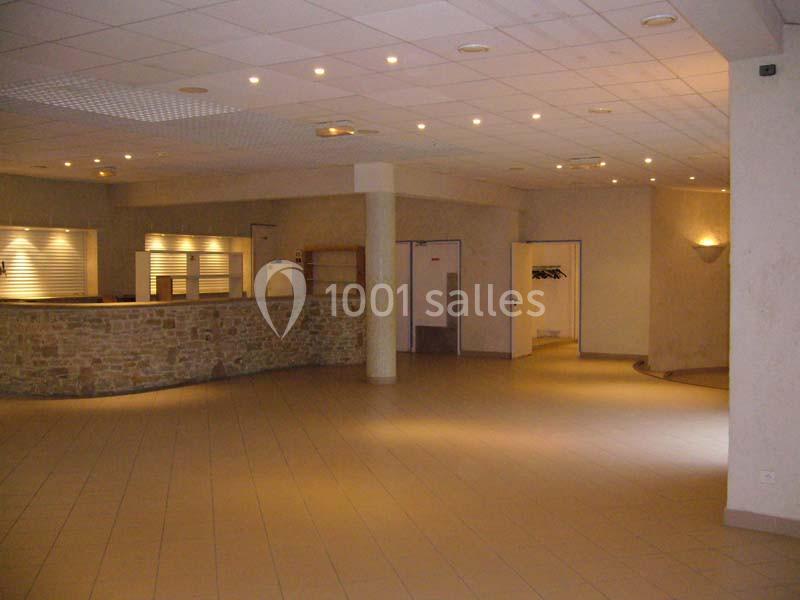 Salle vide avec comptoir en pierre, sol carrelé beige, murs clairs et éclairage encastré au plafond.