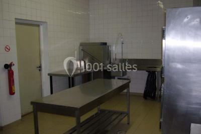 Cuisine professionnelle avec plan de travail en inox, cuisinières, hotte d'extraction et murs carrelés blancs.