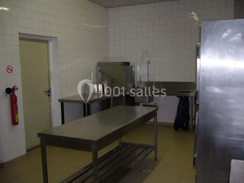 Cuisine professionnelle avec plans de travail en acier inoxydable, évier, carrelage blanc et extincteur mural.