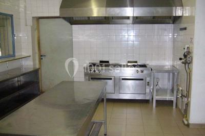 Cuisine professionnelle avec plan de travail en inox, cuisinières, hotte d'extraction et murs carrelés blancs.