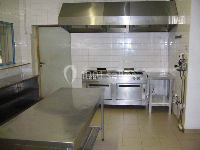 Cuisine professionnelle avec plan de travail en inox, cuisinières, hotte d'extraction et murs carrelés blancs.