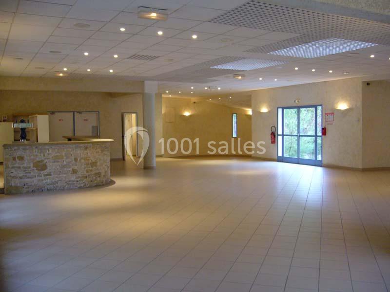 Salle spacieuse avec sol carrelé, murs clairs, comptoir en pierre et grandes fenêtres laissant entrer la lumière naturelle.