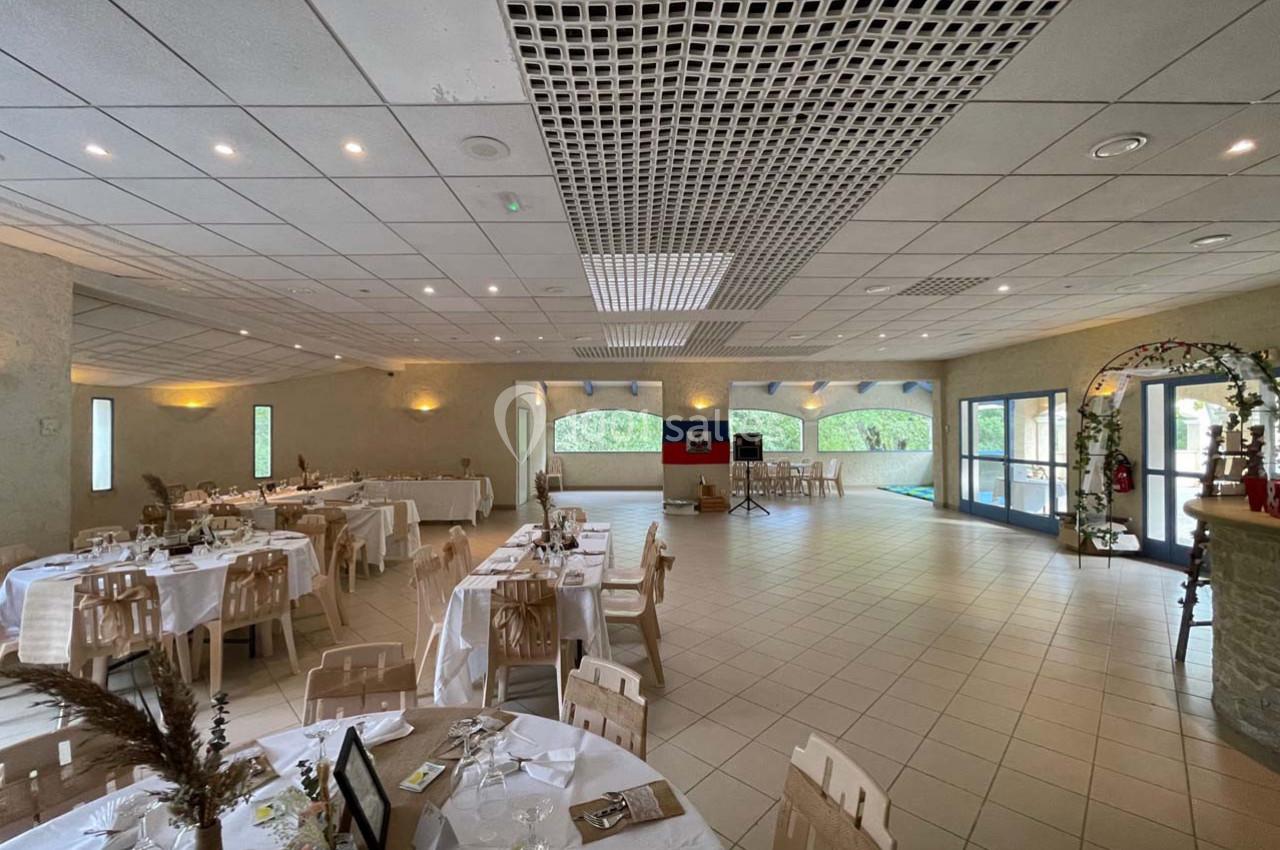 Salle de réception lumineuse avec tables dressées, décorations élégantes et grandes baies vitrées donnant sur l'extérieur.