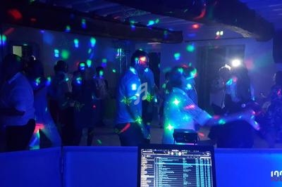Des personnes dansent sous des lumières colorées dans une salle sombre, vue depuis une table de mixage.