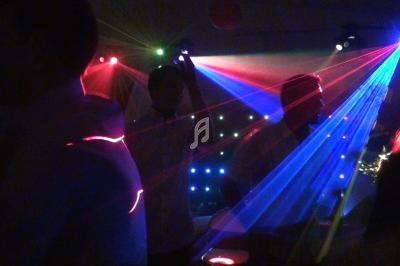 Personnes dansant dans une ambiance sombre avec des faisceaux lumineux colorés et des jeux de lumière.